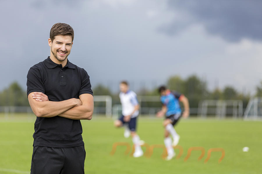 Portrait of smiling coach with soccer players in background Photograph by Westend61
