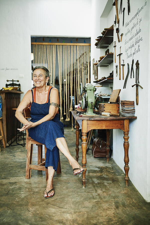 Portrait of smiling female shoemaker sitting at worktable in workshop Photograph by Thomas Barwick