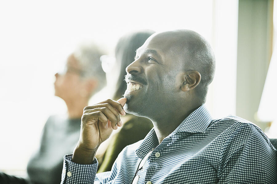 Portrait of smiling mature businessman listening during meeting with coworkers Photograph by Thomas Barwick