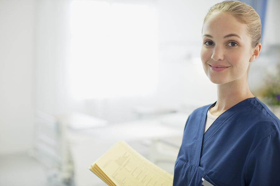 Portrait of smiling nurse holding medical record in hospital room Photograph by Sam Edwards