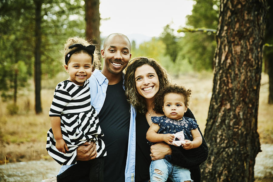 Portrait of smiling parents holding two young daughters Photograph by Thomas Barwick