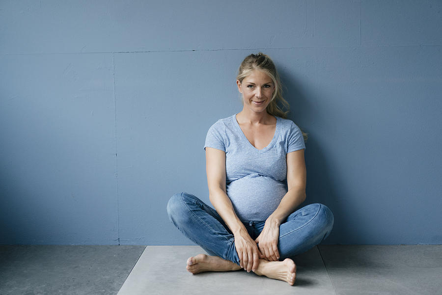 Portrait of smiling pregnant woman sitting on the floor Photograph by Westend61