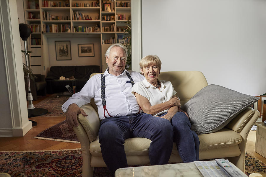 Portrait of smiling senior couple sitting on couch at home Photograph by Oliver Rossi
