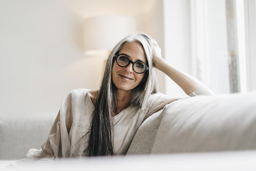 Portrait of smiling woman with long grey hair sitting on the couch Photograph by Westend61