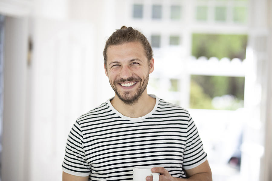 Portrait of smiling young man holding cup of coffee at home Photograph by Westend61