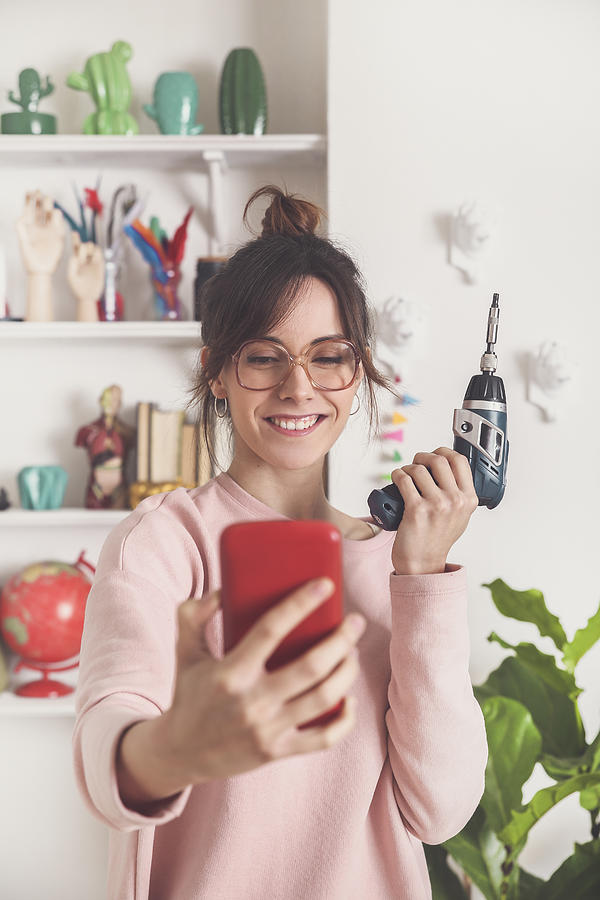 Portrait of smiling young woman taking selfie with electric screwdriver at home Photograph by Westend61