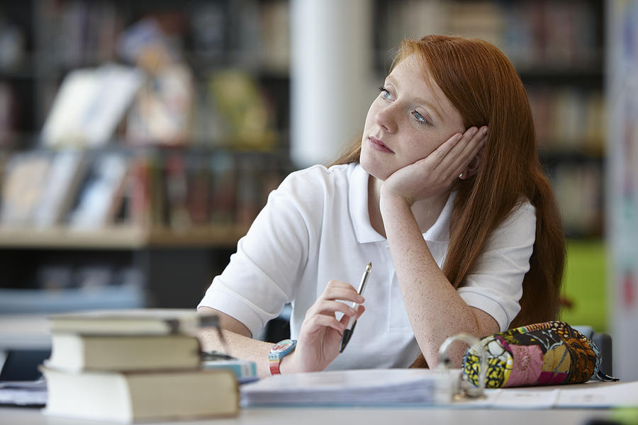 Portrait of teenage girl daydreaming in library Photograph by Phil Boorman