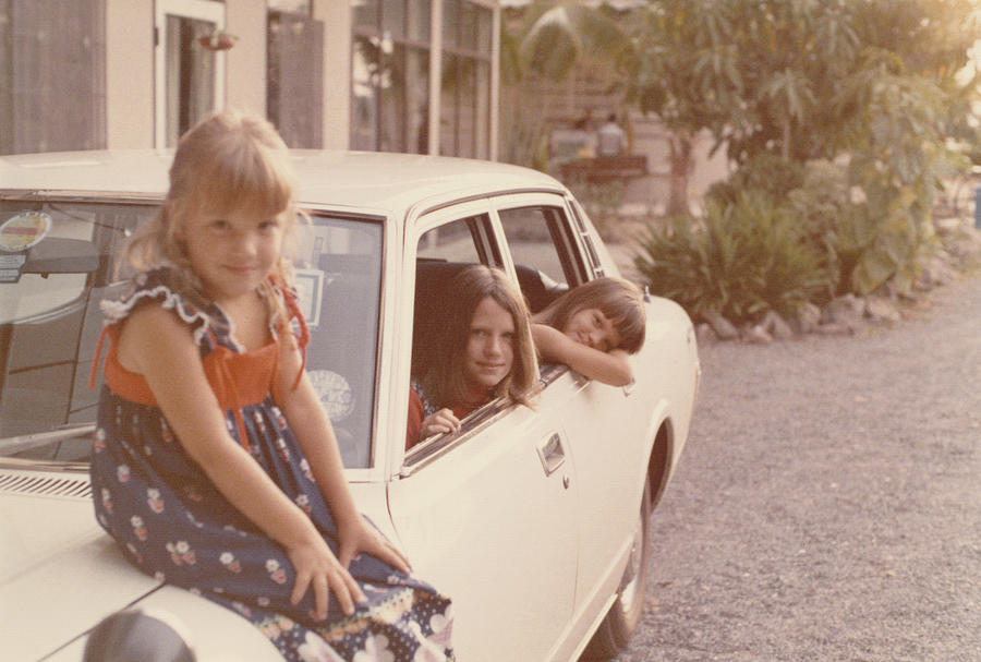 Portrait of Three Girls, One Sitting on a Car Bonnet, Two Others Inside the Car Photograph by Digital Vision.