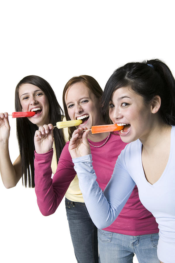 Portrait of three teenage girls eating ice lollies Photograph by Photodisc