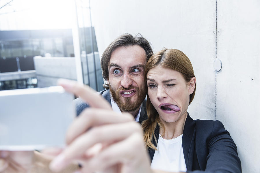 Portrait of two business people making faces while taking a selfie with smartphone Photograph by Westend61
