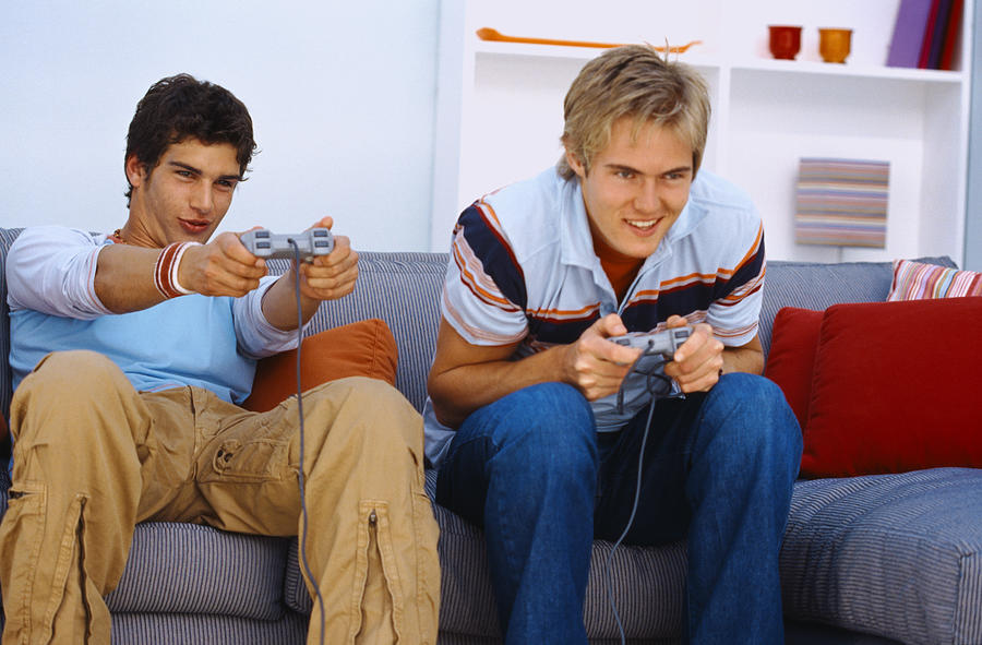 Portrait of two young men sitting on a couch and playing a video game Photograph by Stockbyte