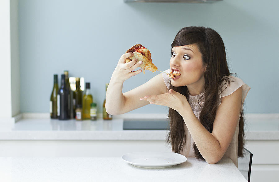 Portrait of woman eating pizza Photograph by Flashpop