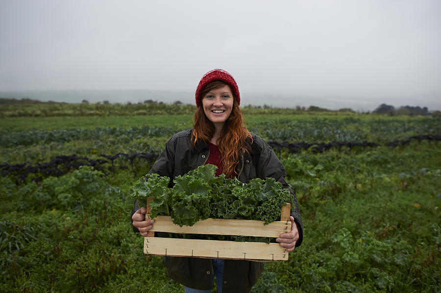 Portrait of woman holding box of kale on farm. Photograph by Dougal Waters