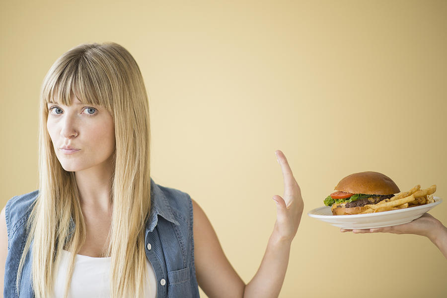 Portrait of woman rejecting hamburger that is being offered to her Photograph by Jamie Grill