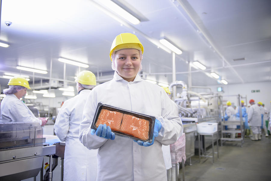 Portrait of worker holding pack of salmon fillets in food factory Photograph by Monty Rakusen