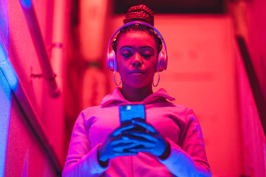 Portrait of young black woman listening to music under neon lights Photograph by Recep-bg