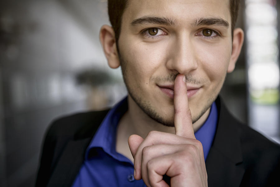 Portrait of young businessman with finger on lips in office Photograph by Suedhang