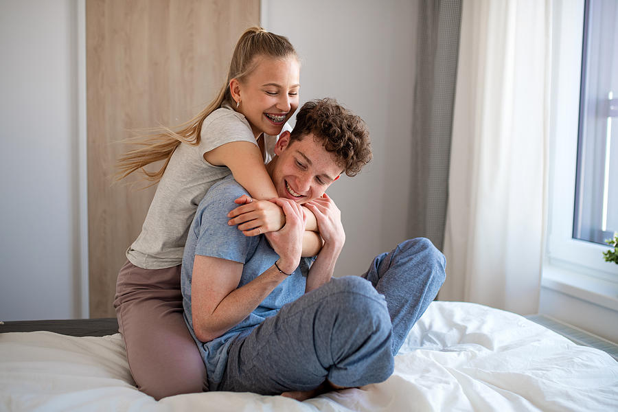Portrait of young couple indoors at home, having fun on bed. Photograph by Halfpoint Images