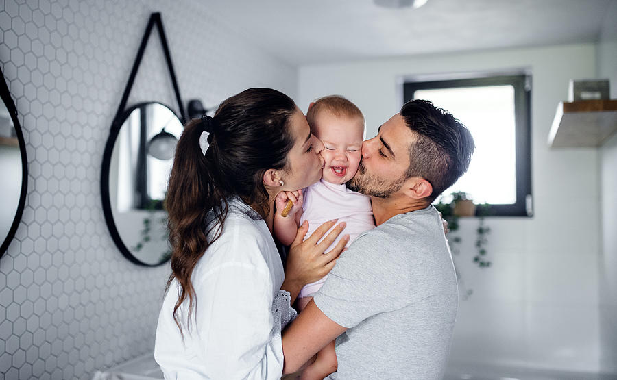 Portrait of young couple with toddler girl in the morning indoors in bathroom at home, kissing. Photograph by Halfpoint Images