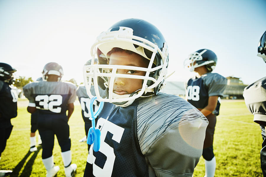 Portrait of young football player standing on field with teammates before game Photograph by Thomas Barwick
