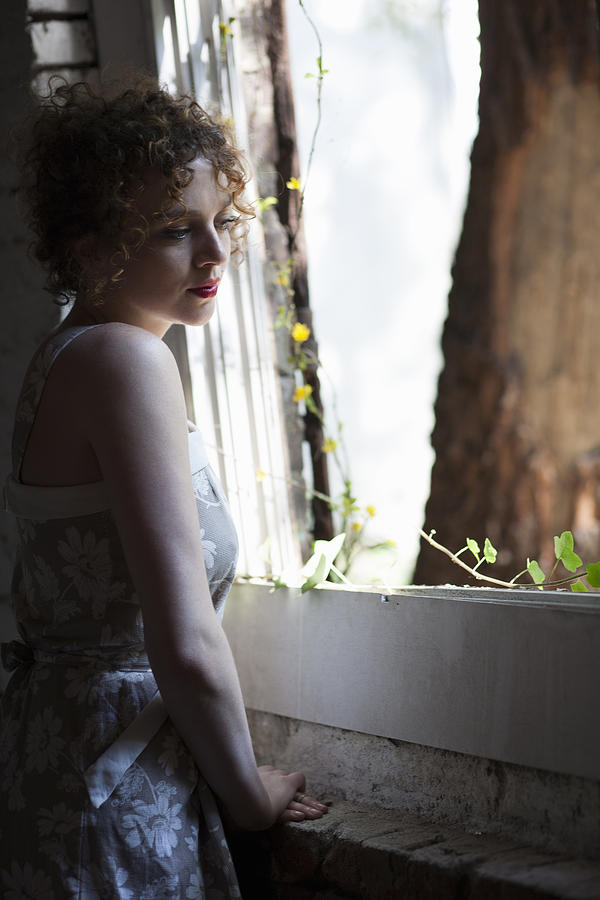 Portrait of young woman daydreaming at conservatory window Photograph by Ashley Corbin-Teich