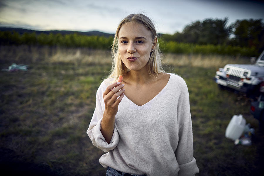 Portrait of young woman eating a carrot in the countryside Photograph by Oliver Rossi