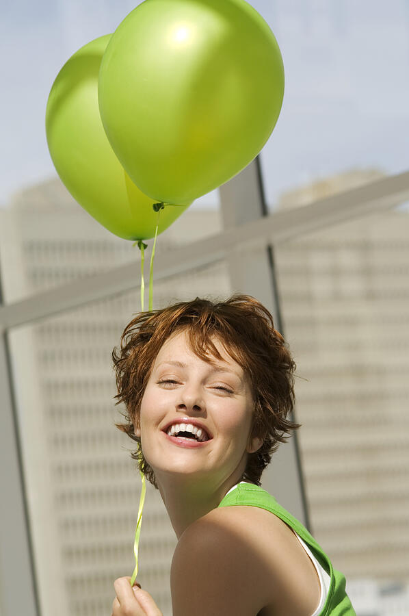 Portrait of young woman holding green balloons Photograph by A. Chederros