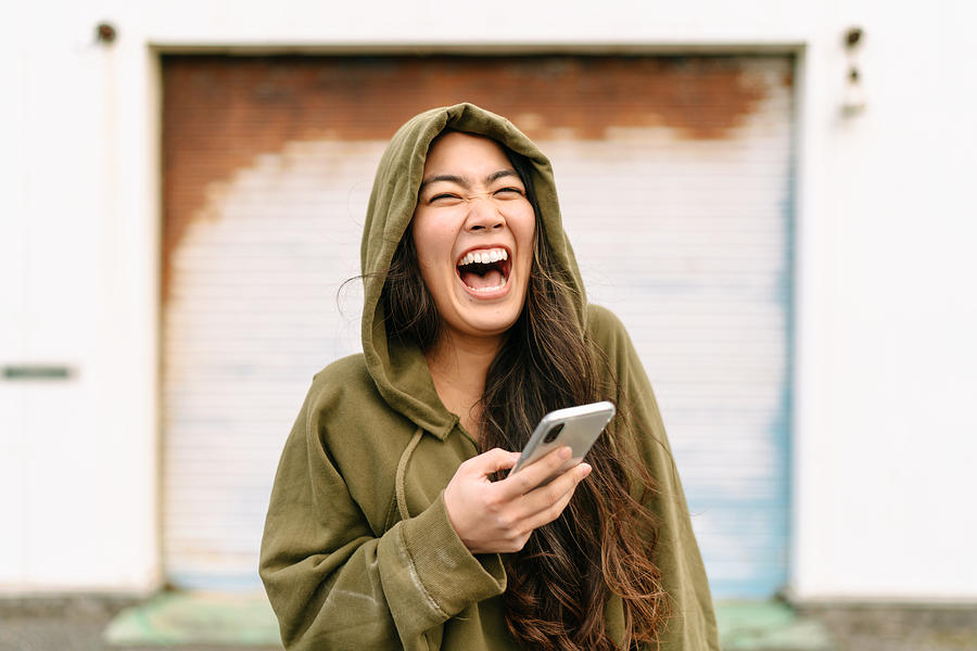 Portrait of young woman holding smart phone and laughing Photograph by Recep-bg