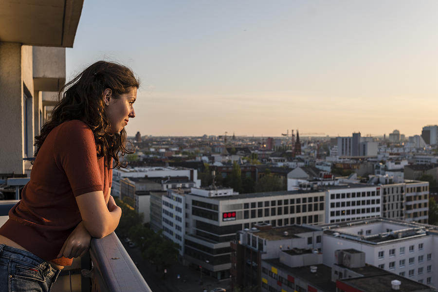 portrait of young woman leans at balcony and looks over Berlin skyline while sunset Photograph by Fotografixx
