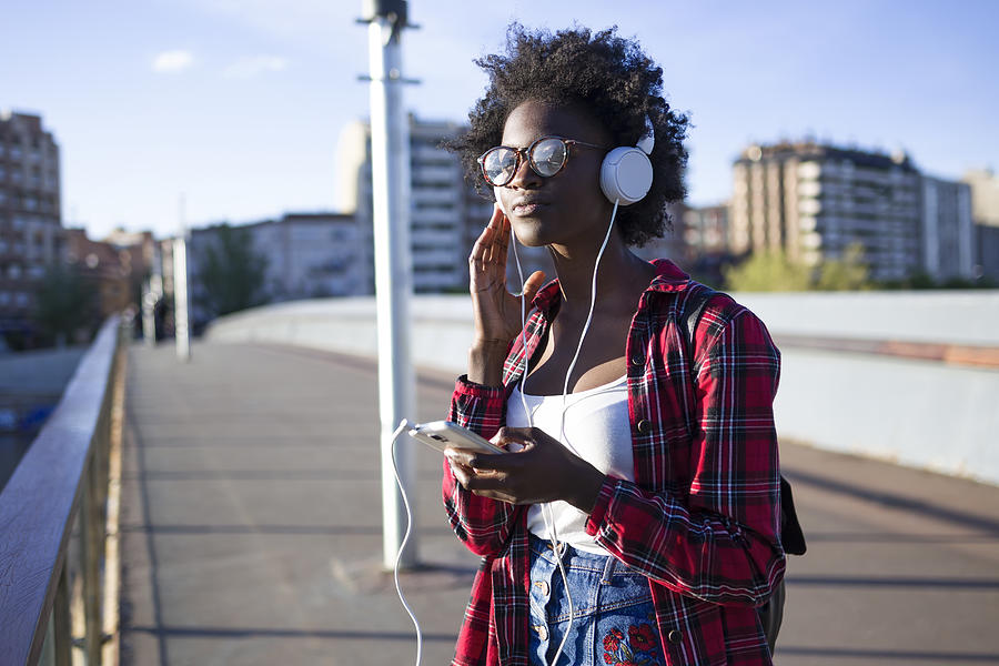 Portrait of young woman on a bridge listening music with headphones Photograph by Westend61