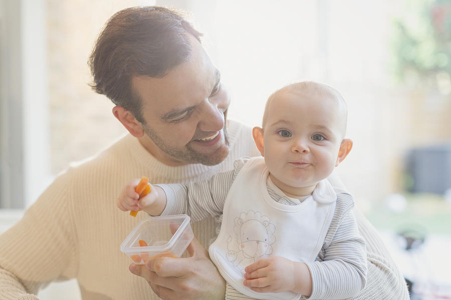 Portrait smiling, cute baby son and father eating carrots Photograph by Caia Image