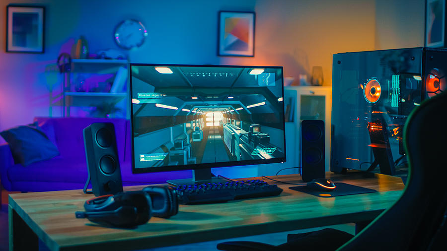 Powerful Personal Computer Gamer Rig with First-Person Shooter Game on Screen. Monitor Stands on the Table at Home. Cozy Room with Modern Design is Lit with Warm and Neon Light. Photograph by Gorodenkoff
