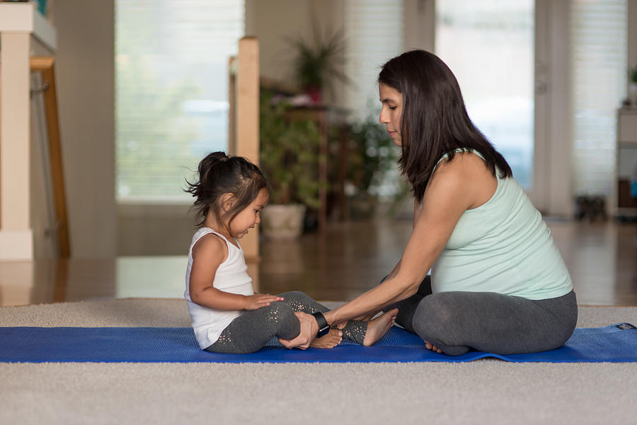 Pregant ethnic mother doing yoga with her young toddler girl Photograph by FatCamera