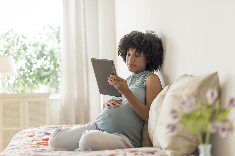 Pregnant African American mother using digital tablet in bed Photograph by JGI/Tom Grill