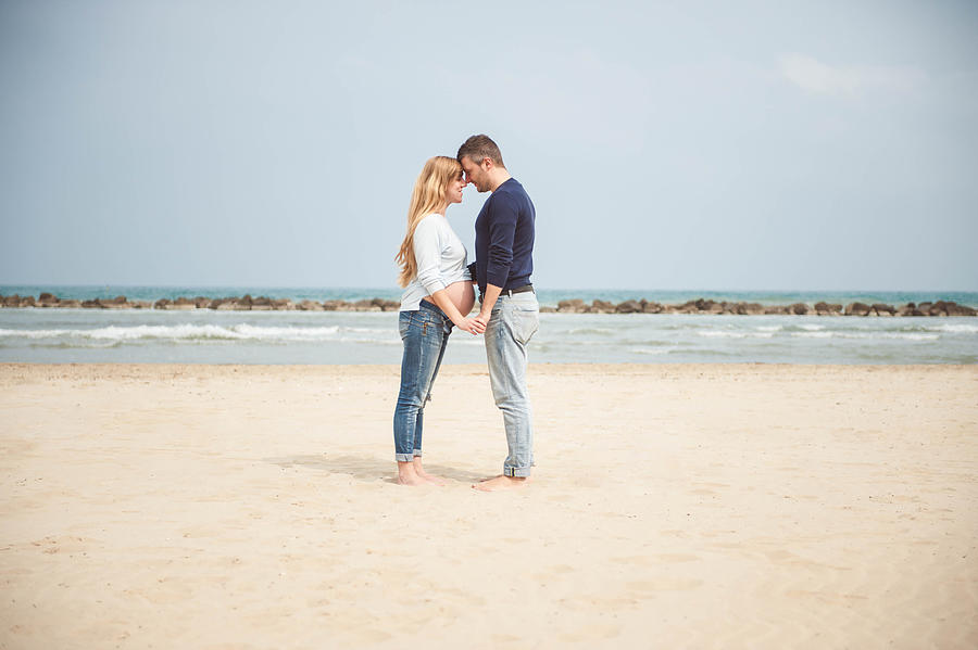 Pregnant couple on the beach. Hand in hand. Casual clothes. Photograph by © Samantha Carrirolo