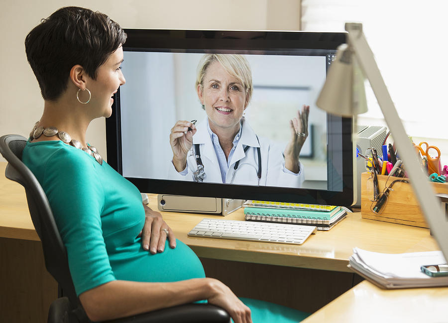Pregnant mixed race businesswoman video chatting with doctor Photograph by Ariel Skelley