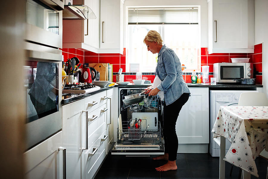 Pregnant woman emptying the dishwasher Photograph by Dean Mitchell