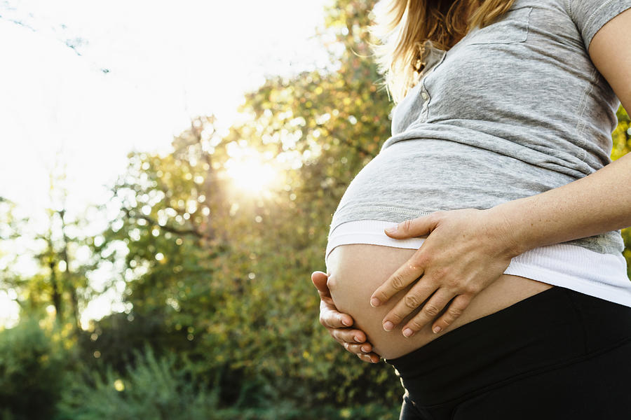 Pregnant woman holding belly, outdoors, mid section Photograph by Julian Rupp
