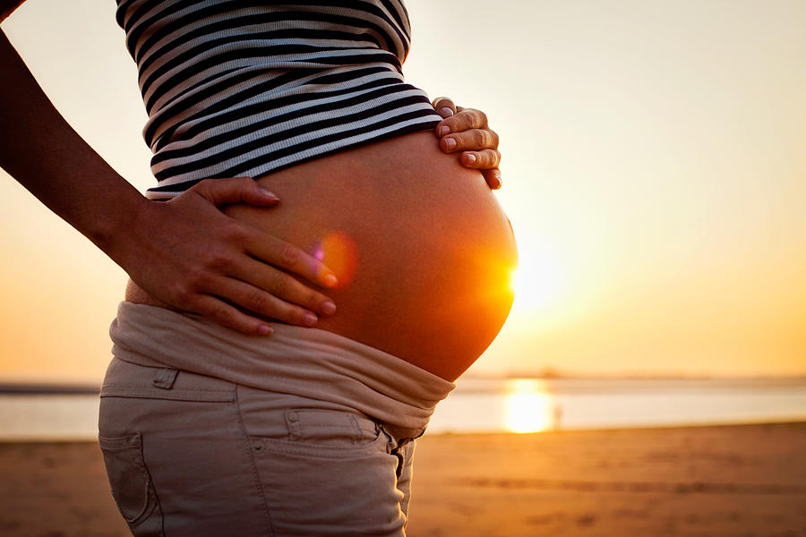 Pregnant woman holding bump on beach at sunset. Photograph by Tim Robberts