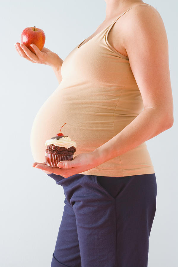 Pregnant woman holding healthy and unhealthy snacks Photograph by Jennifer L. Boggs