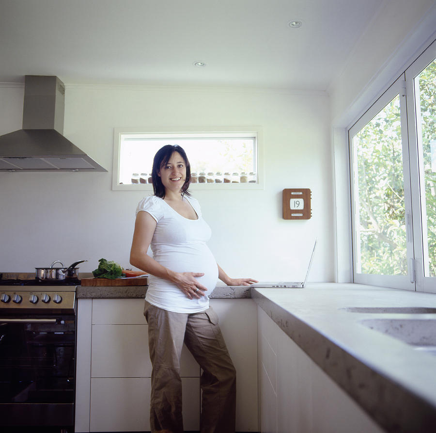 Pregnant woman in kitchen, smiling, portrait Photograph by Heidi Coppock-Beard