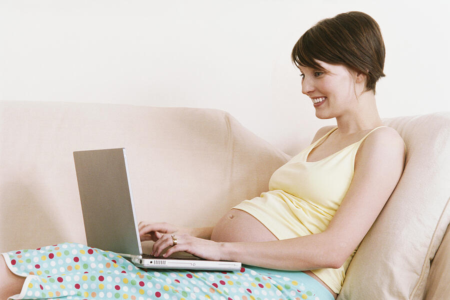 Pregnant Woman Sits on a Sofa Using a Laptop Photograph by Nancy Ney