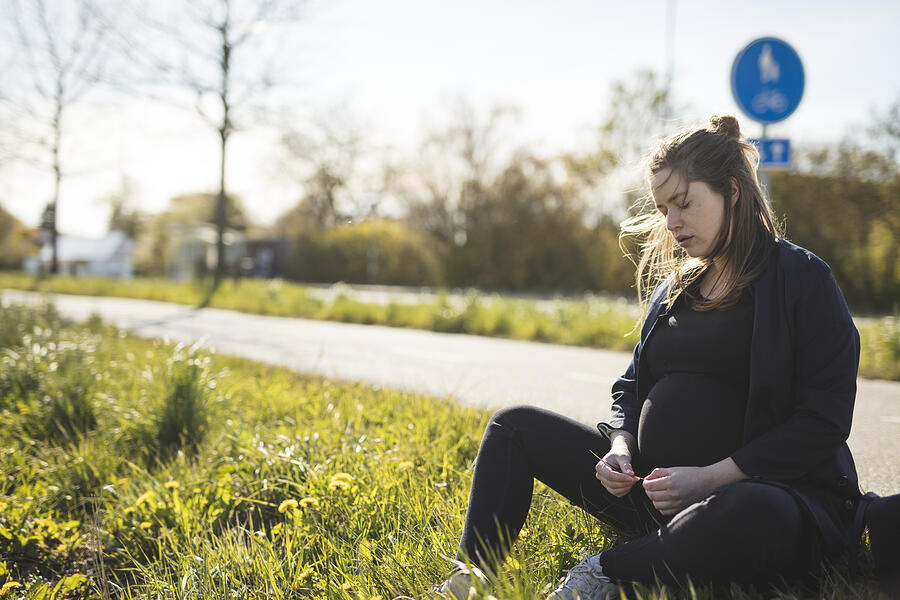 Pregnant woman sitting at roadside Photograph by Johner Images