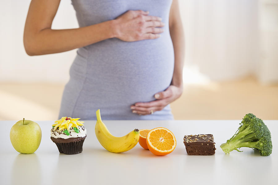 Pregnant woman standing behind a row of food Photograph by Tetra Images