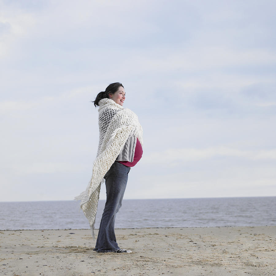 Pregnant woman standing on beach with arms crossed, side view Photograph by Dougal Waters