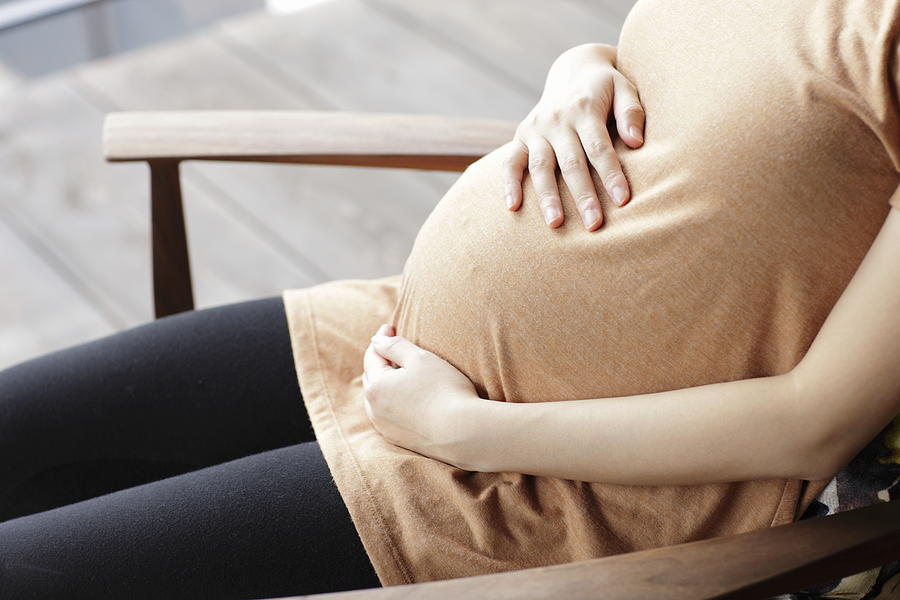 Pregnant woman touching abdomen sitting chair Photograph by Sot