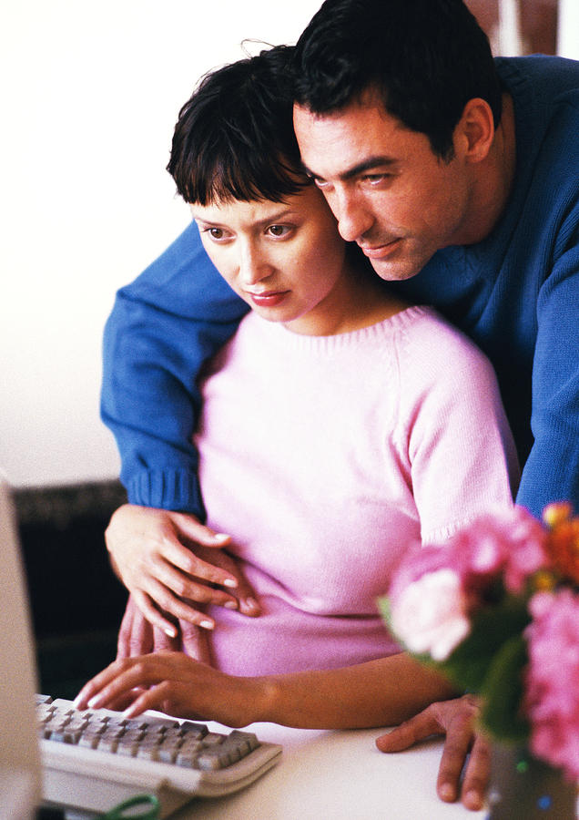 Pregnant woman using computer, man hugging her Photograph by John Dowland