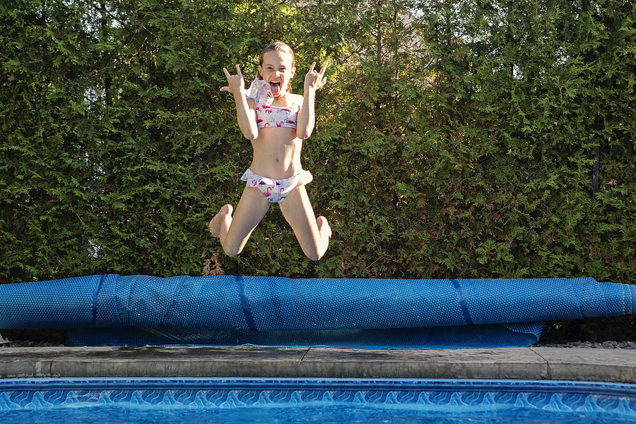 Preteen girl jumping in backyard pool making a face. Photograph by Martinedoucet