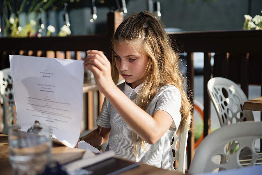 Preteen girl looking at the menu at restaurant terrace. Photograph by Martinedoucet