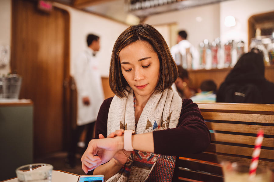 Pretty young lady waiting and using her smartwatch joyfully in the restaurant Photograph by Images By Tang Ming Tung